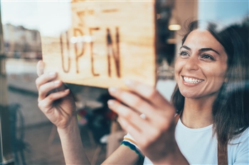 Woman in storefront flipping the "open" sign on the door