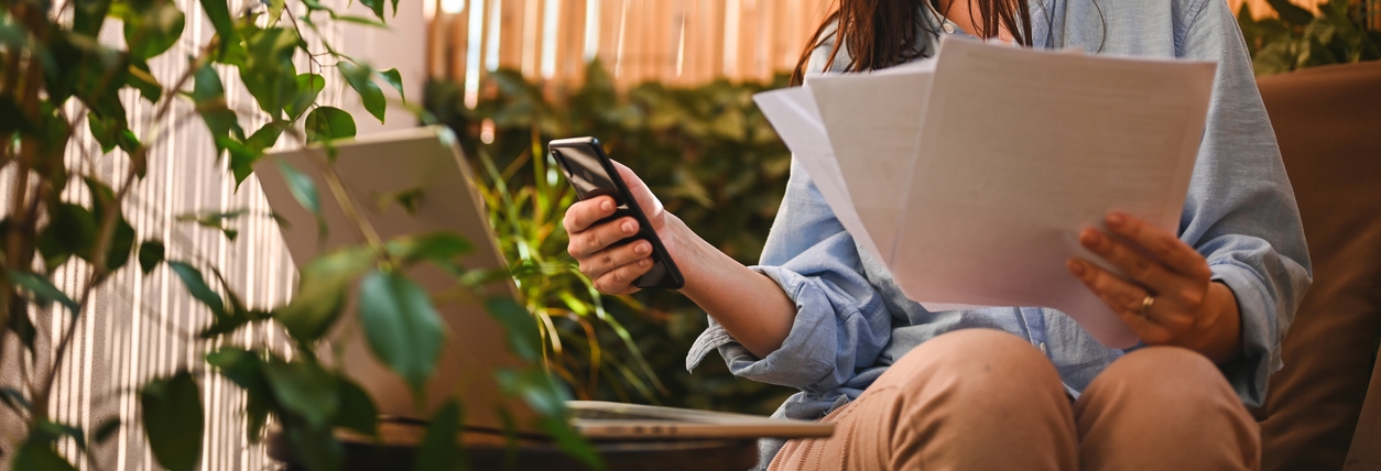 Woman looking at phone, computer, and holding a piece of paper