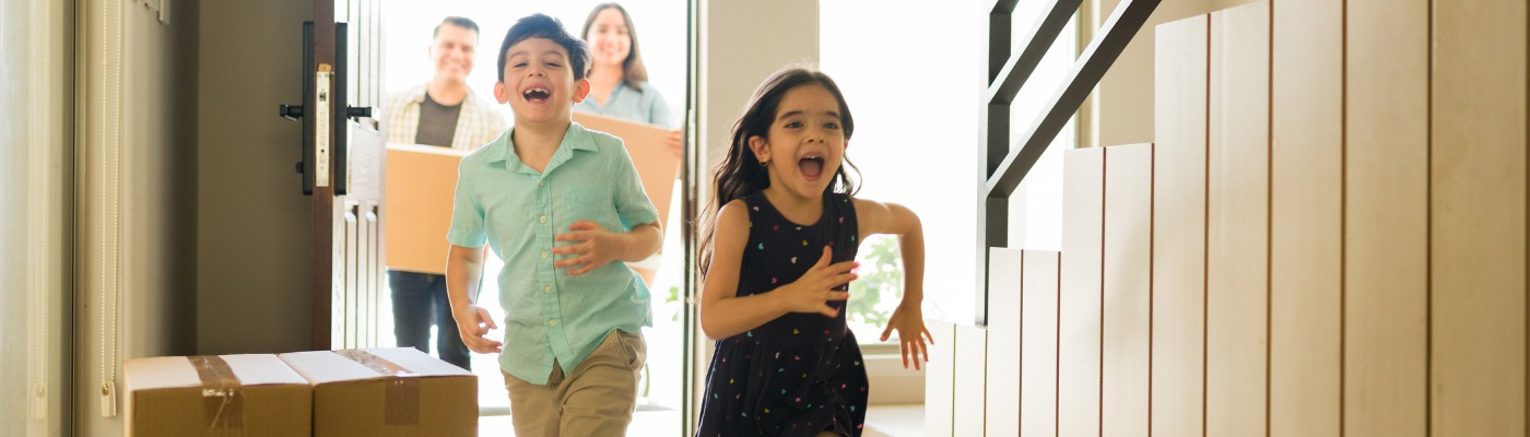 boy and girl running into new house with parents behind them carrying boxes